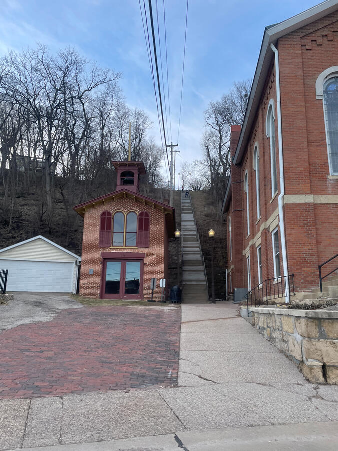 Alleys between brick buildings reveal the working infrastructure behind Galena’s historic storefronts. Narrow brick alleyway in Galena, Illinois, showing historic multi‑story brick buildings, a red‑brick street transition, and a small cupola‑topped structure framed by leafless hillside trees under a clear sky.