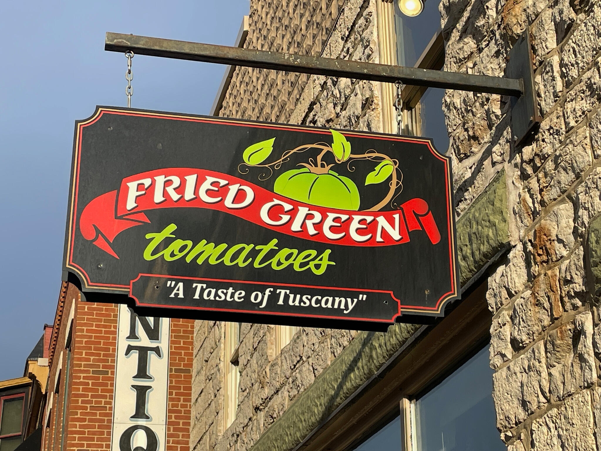 fried-green-tomatoes-sign-galena-illinois Vintage-style wooden restaurant sign for Fried Green Tomatoes featuring a red banner, green script lettering, and the tagline "A taste of Tuscany" on a black background with a green tomato illustration.