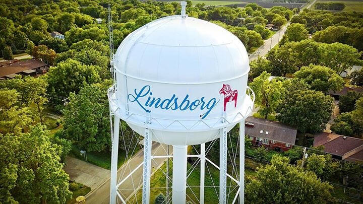 lindsborg-kansas-dala-horse-water-tower-hero Aerial view of the Lindsborg, Kansas water tower featuring a red Dala horse design, surrounded by treetops and neighborhood streets.